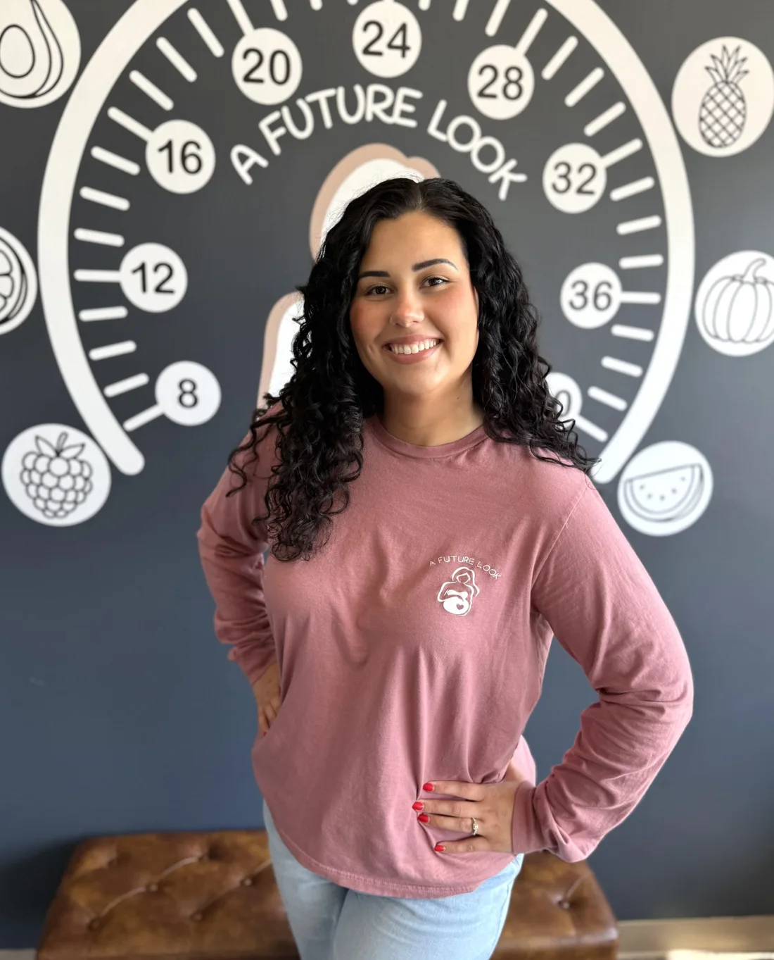 Bailey Rose, sonographer at A Future Look, standing in front of the studio's pregnancy week wall